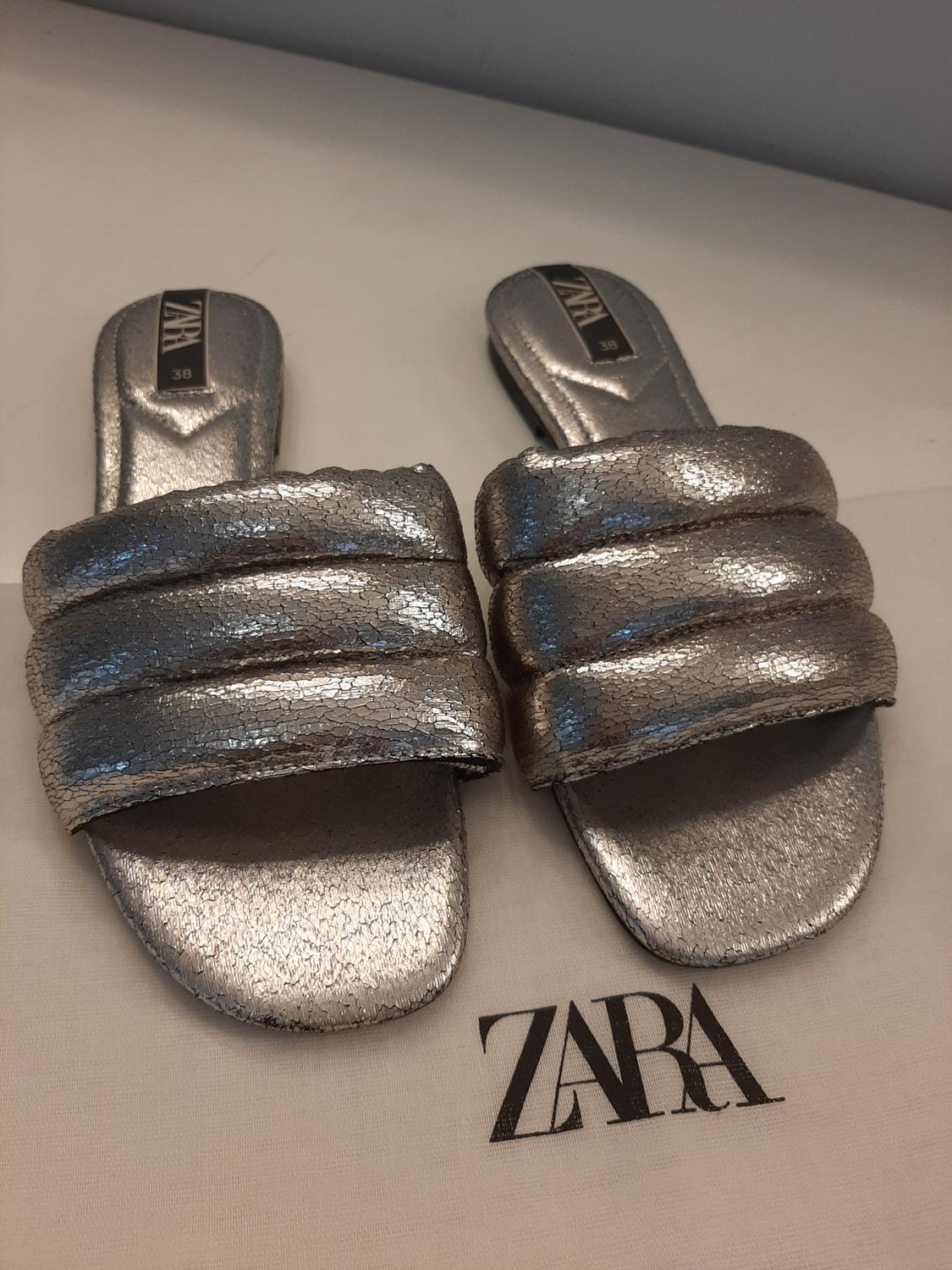 Front view of silver sandals with padded straps on a background with 'ZARA' text.