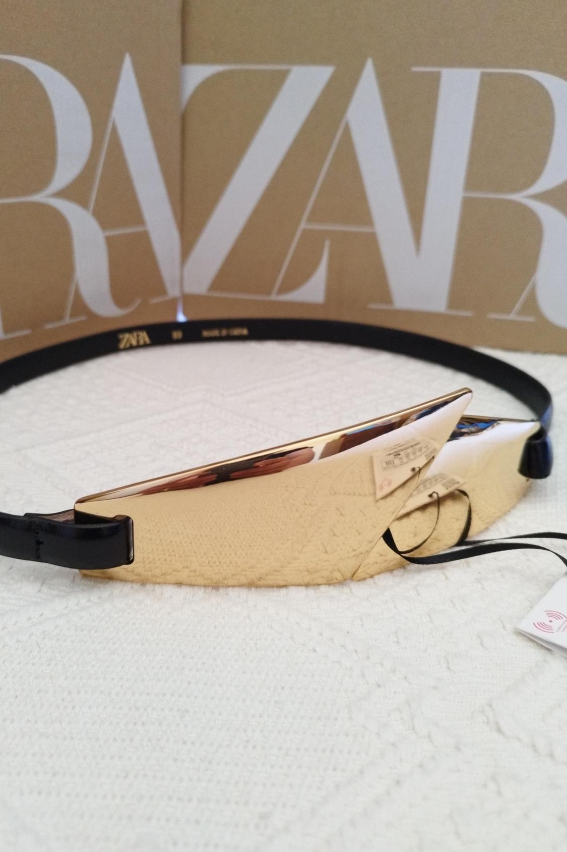 Detail of gold sunglasses with a brown case and visible 'ZARA' text.