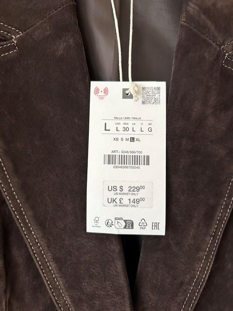 Price tag hanging from a brown jacket with visible stitching. Text on tag: "US $229.00, UK £149.00, L 30 LL G".