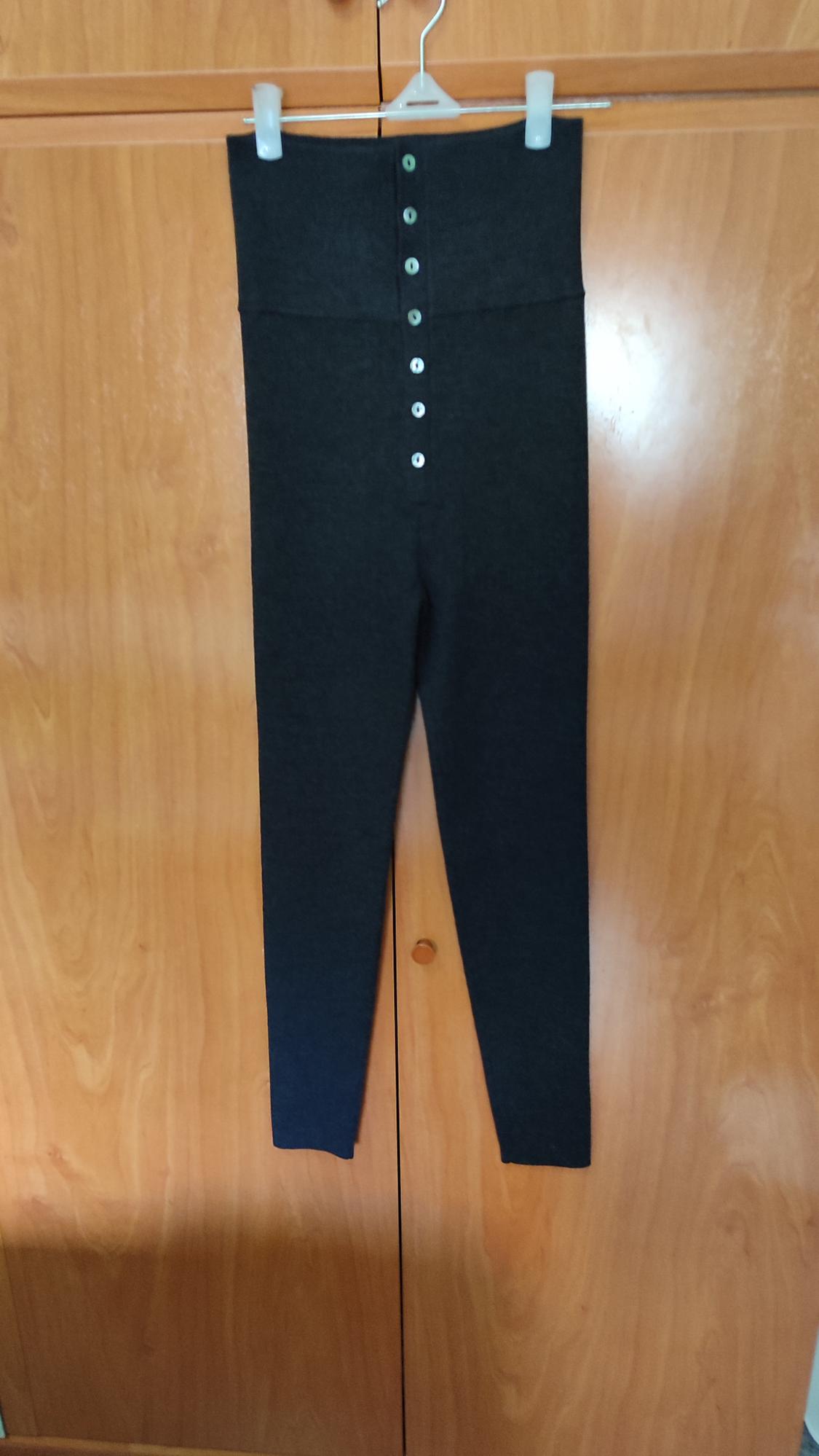 Black high-waisted trousers with front buttons, hanging on a hanger against a light wooden background.