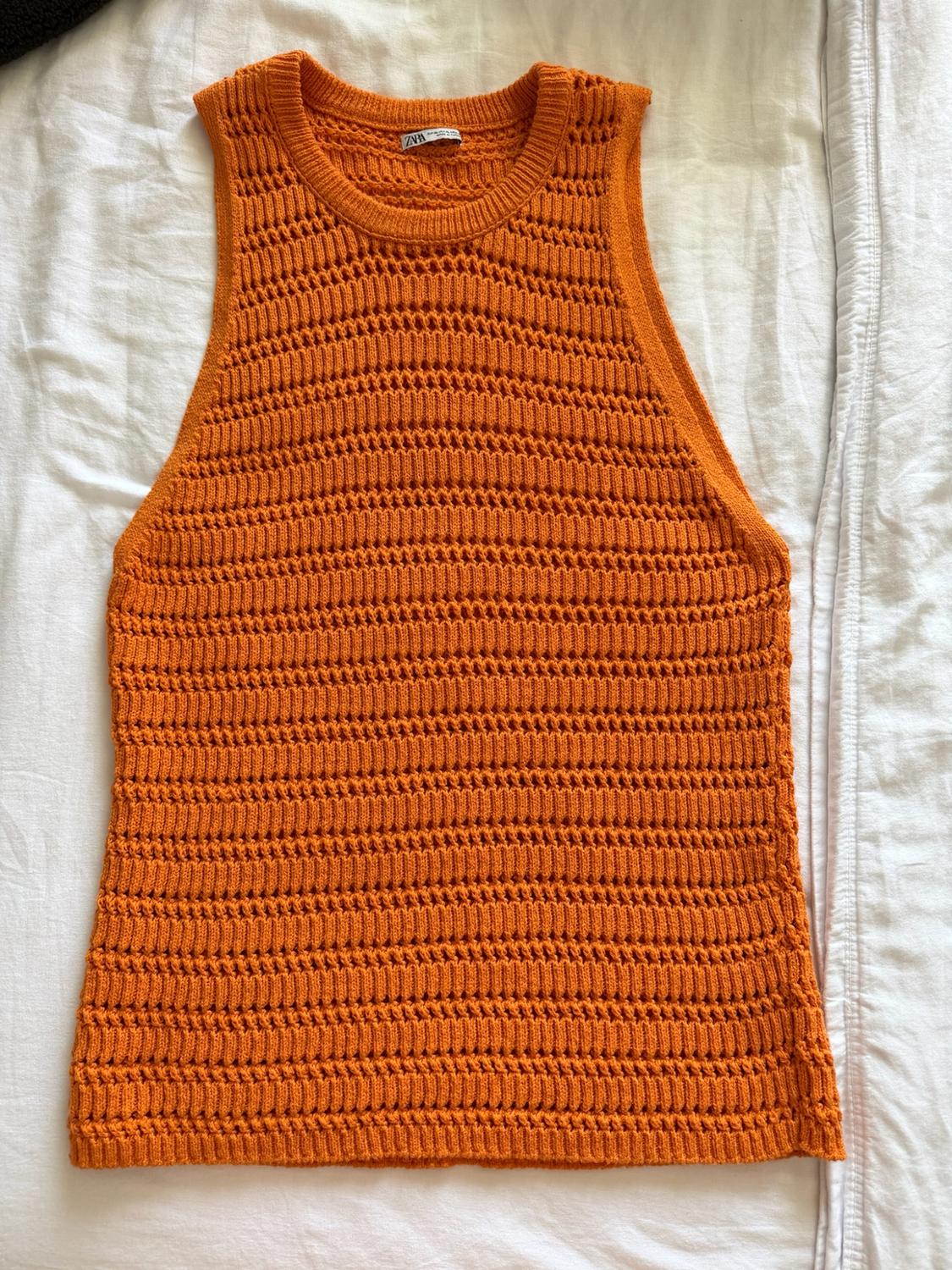 Orange sleeveless open-knit top over a crinkled white fabric. Label featuring the text ZARA on the neck. Relaxed style.