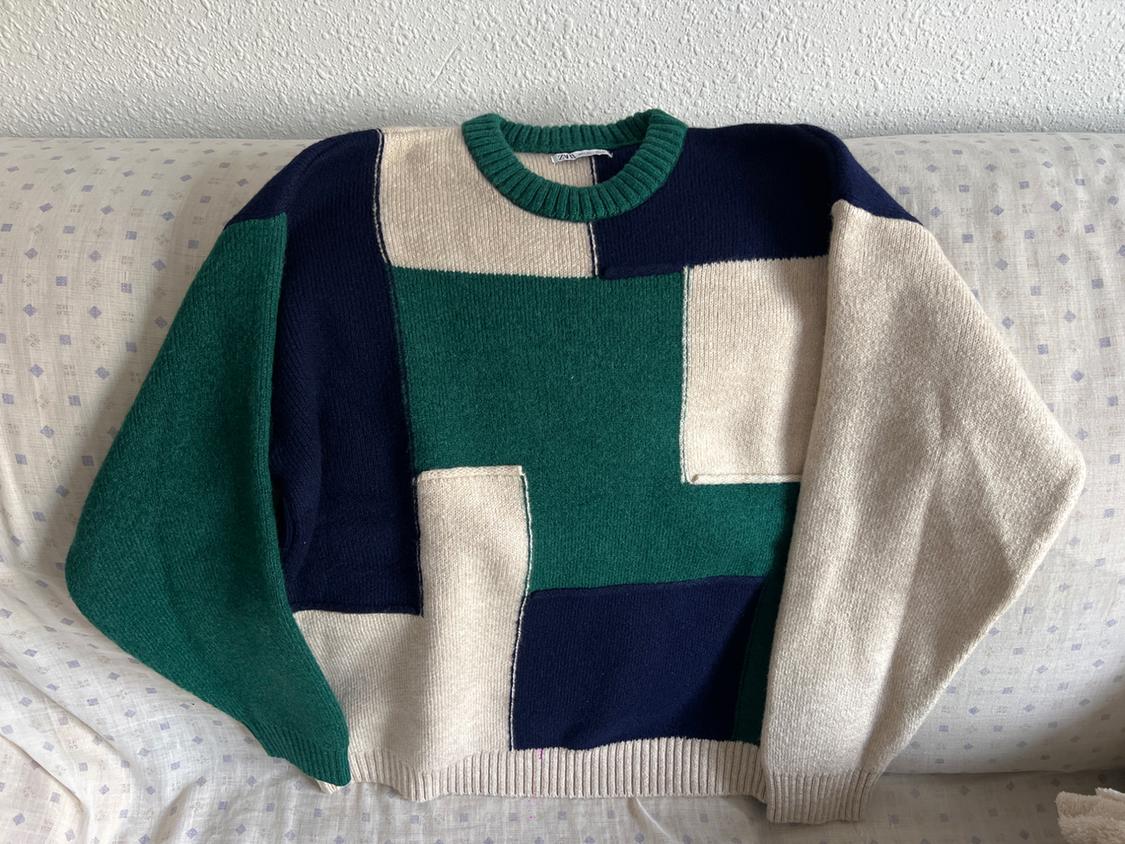 Green, blue, and beige colour-block jumper on a light sofa with a small checked pattern.