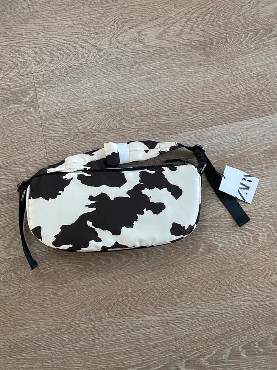 Black and white patterned bag on light wood floor. Visible tag with "ZARA" text in the bottom right corner.