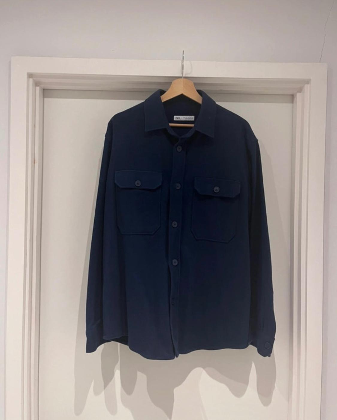Dark blue shirt hanging on a wooden hanger over a white door. It has two front flap pockets.
