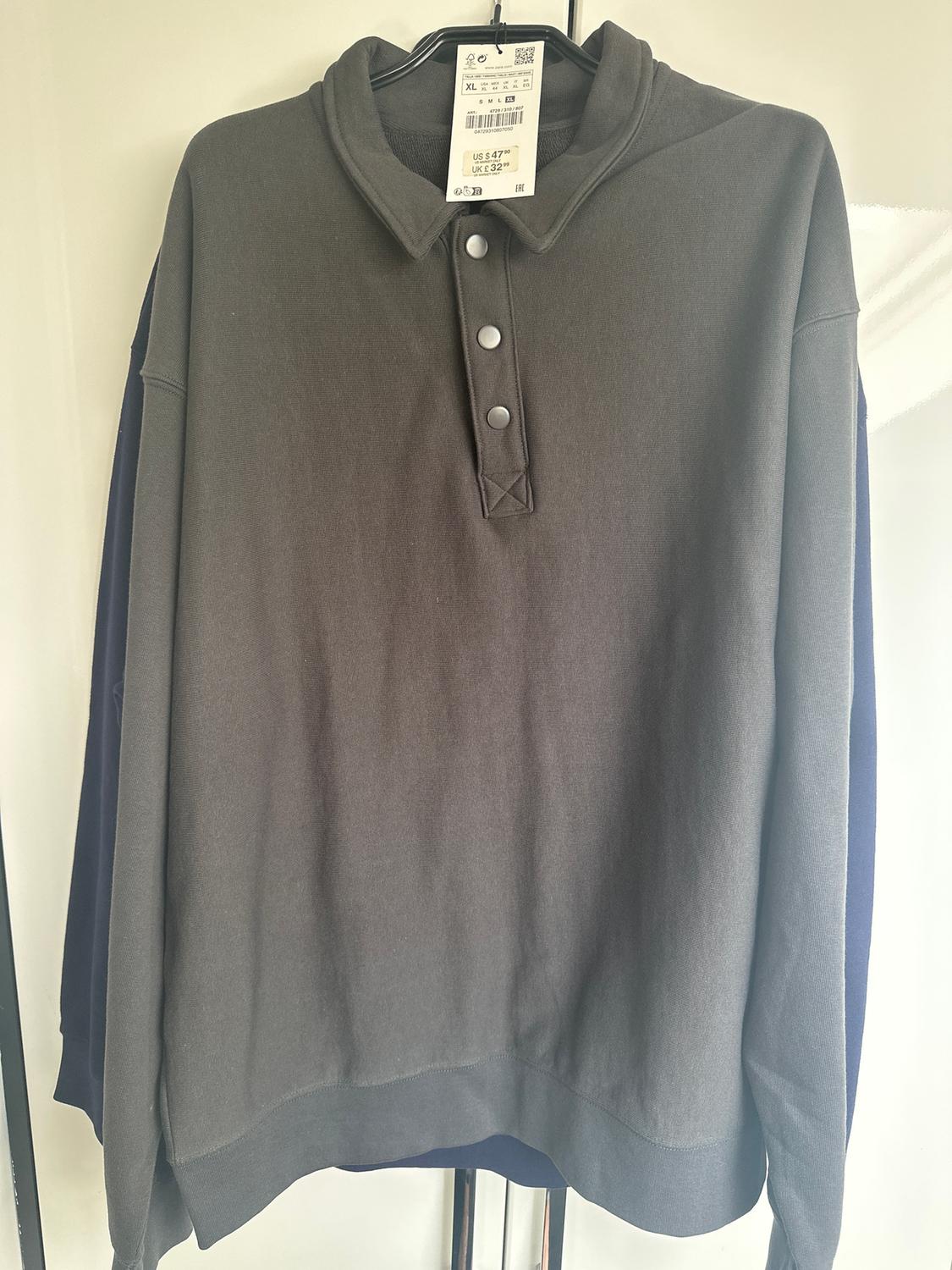 Grey, long-sleeved collared shirt with buttons, hanging on a hanger. Visible tag with price of $5.47 and size XL.