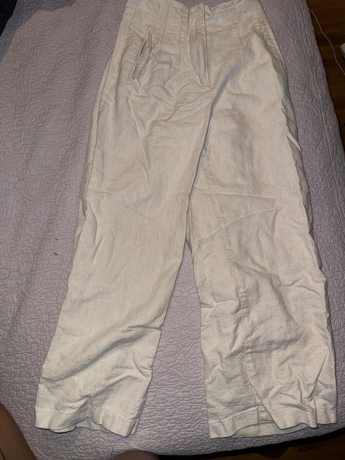 Beige lightweight fabric pants with pockets, placed on a textured gray bedspread.