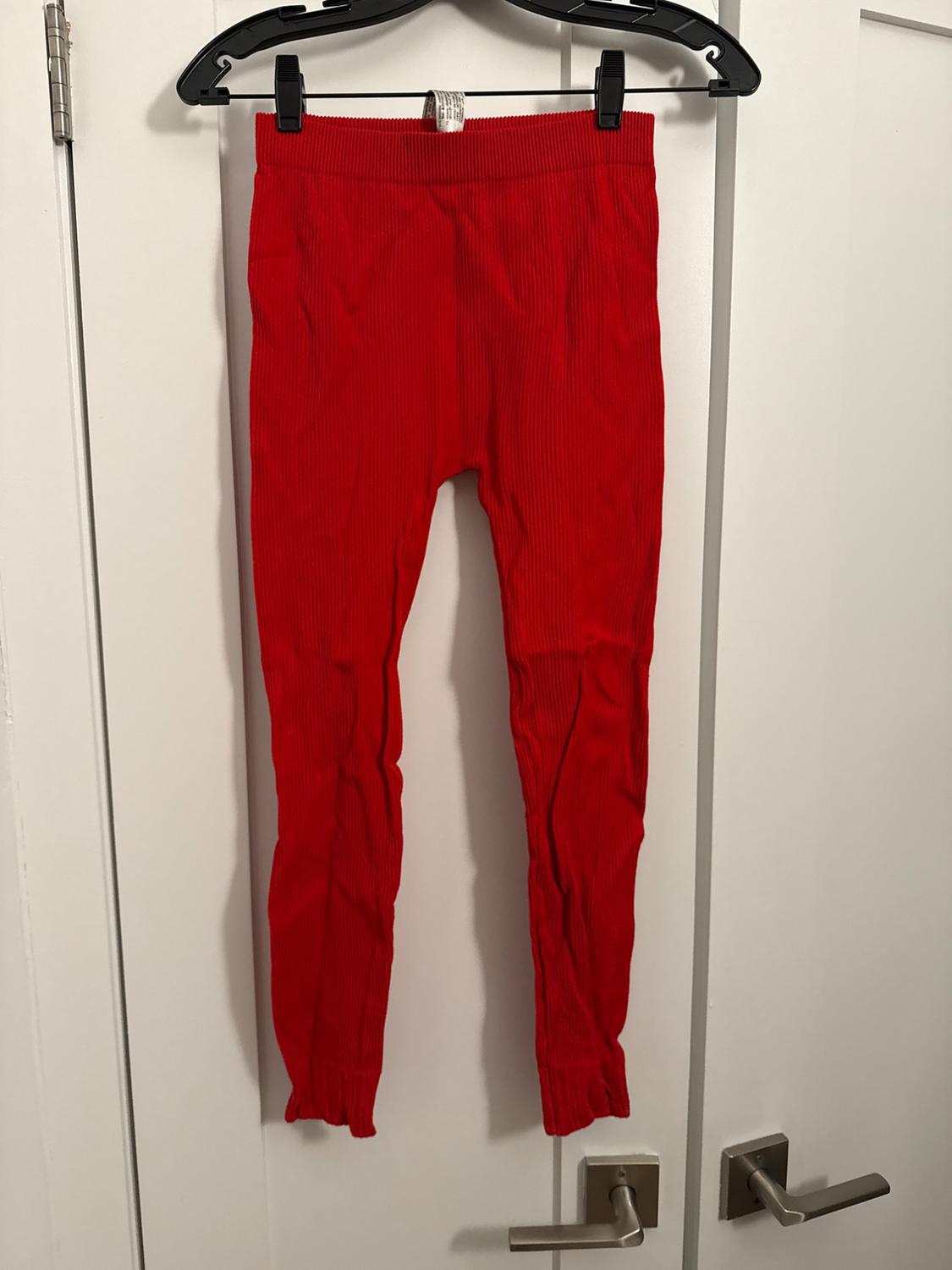 Red pants hanging on a black hanger over a white door. The fabric has a ribbed texture.
