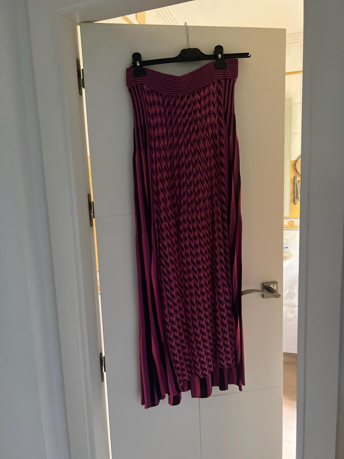 Purple and black maxi skirt with geometric pattern and stripes, hanging on a hanger over an ajar white door in a home.