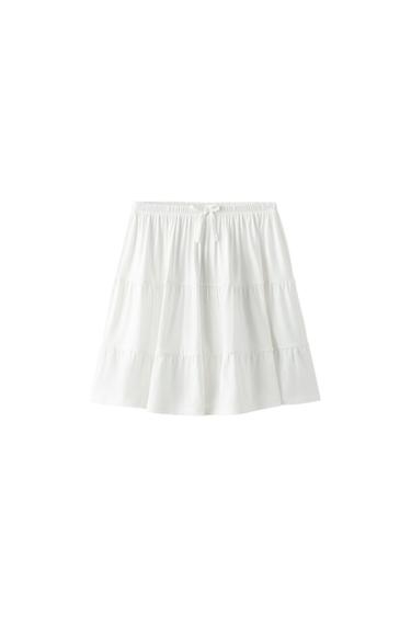 White tiered mini skirt with an elasticated waist and front tie, on a white background.