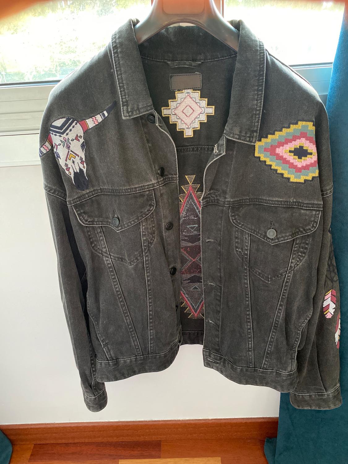 Front view of a black jacket with colourful bull's head embroidery and geometric shapes on the chest and shoulders.