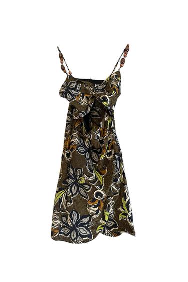 Short dress on a white background. Floral print in brown, black and lime green. Straps with wooden beads and a front knot with an opening.