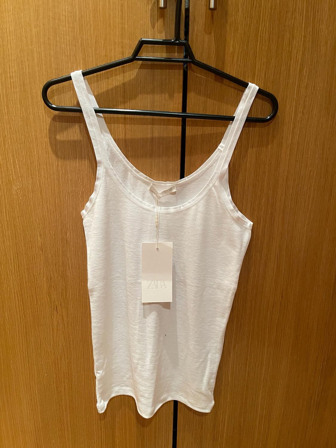White ribbed vest top on a black hanger against a wooden background. Label with the text ZARA.