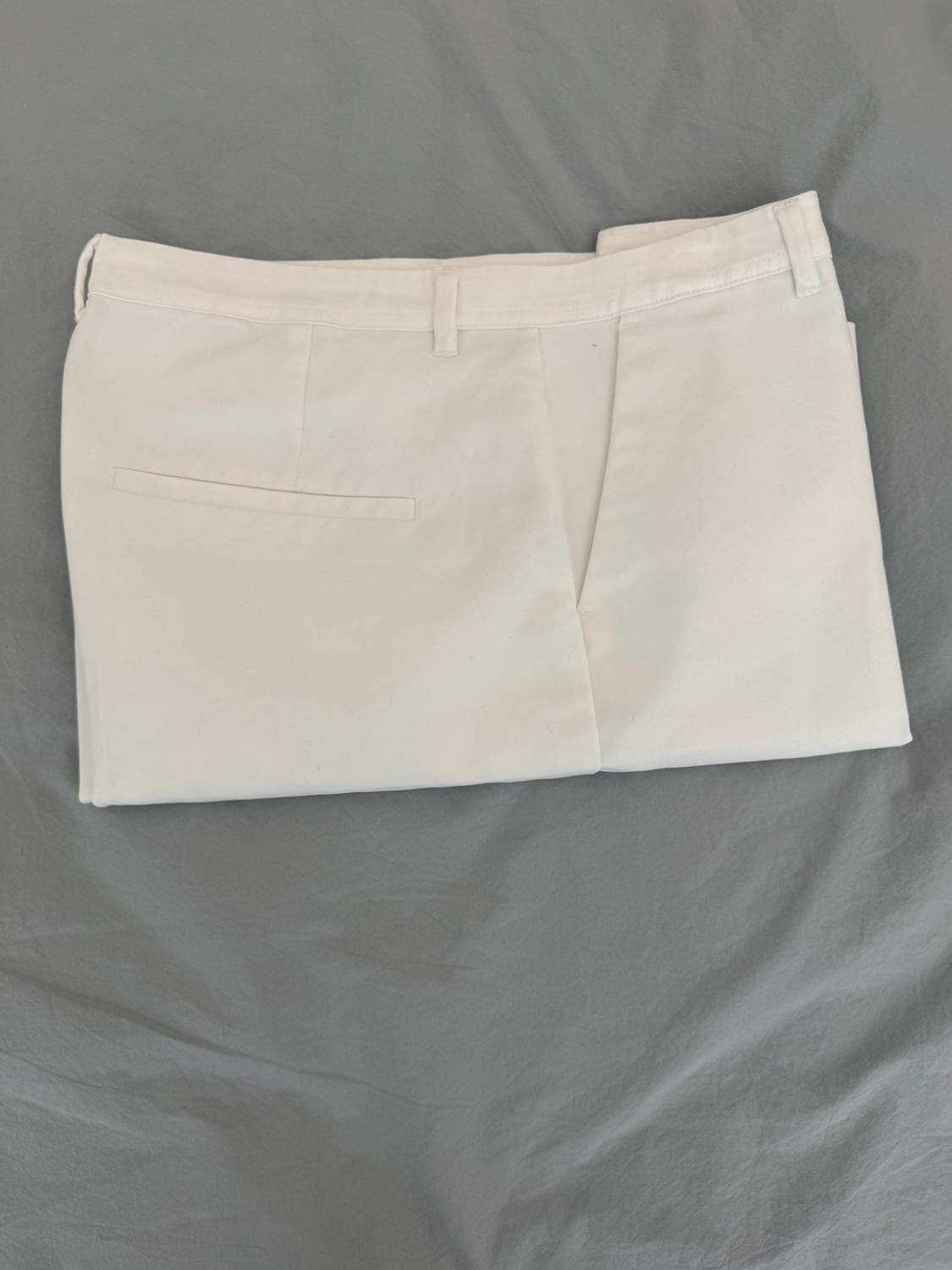 White trousers folded on a grey fabric surface. The waistband with belt loops and a back pocket stand out.