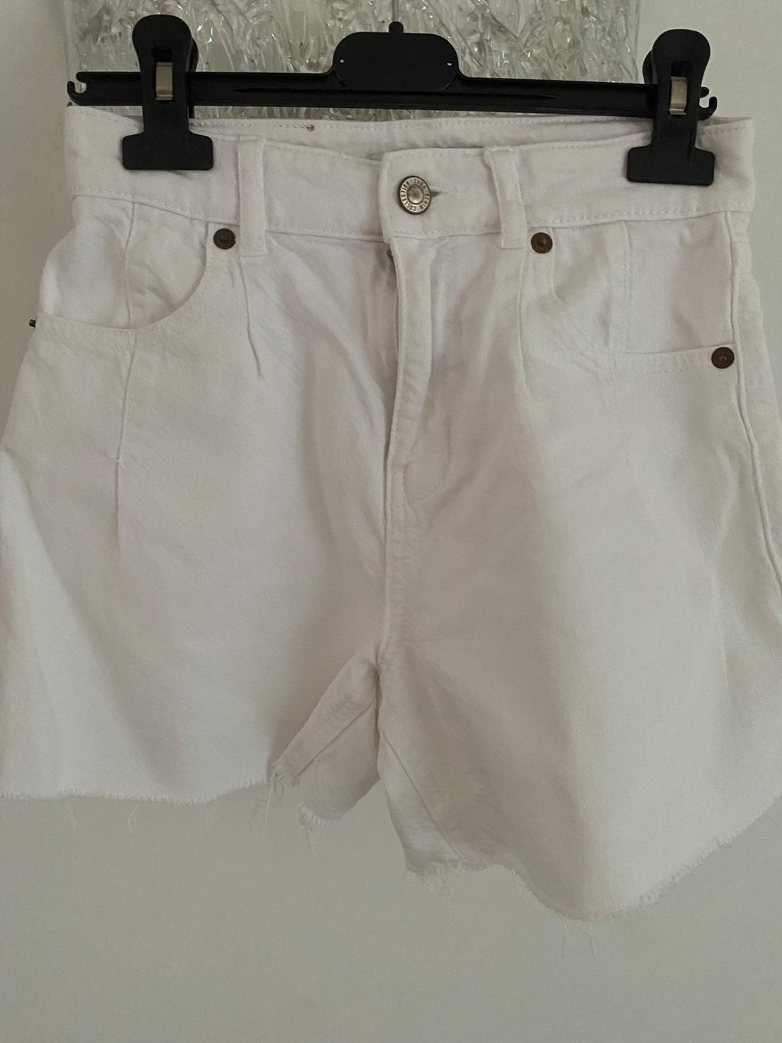 Front view of white shorts with front pockets and a metal button.