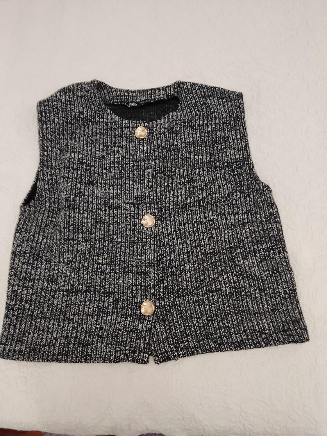 Grey knitted waistcoat with three large buttons on a white surface.