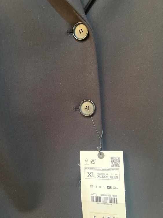 Detail of a black coat with buttons and a price tag. The tag shows size XL and price $129.90.