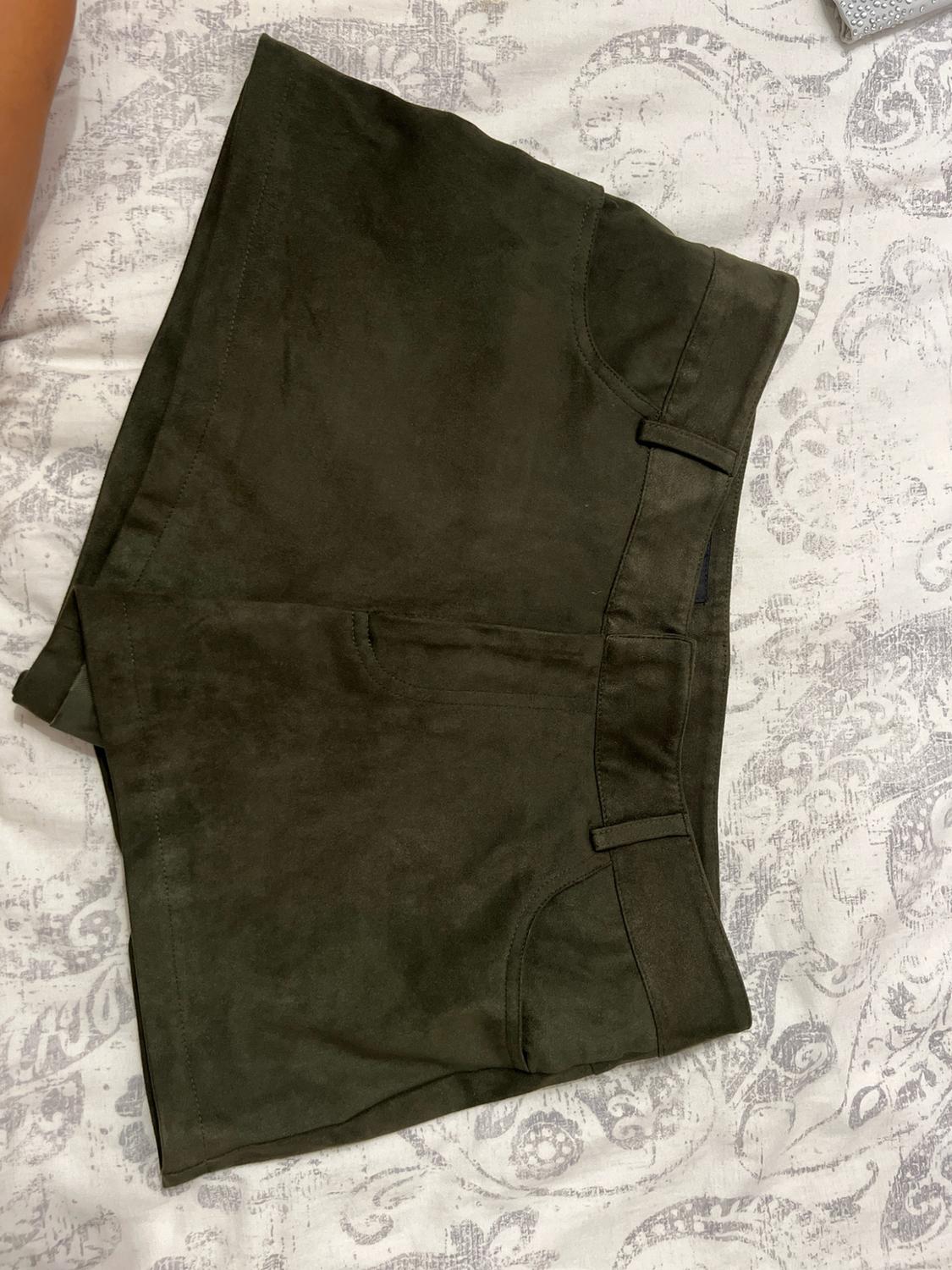 Dark green shorts with pockets and belt loops, on a white sheet with a grey pattern in a relaxed composition.