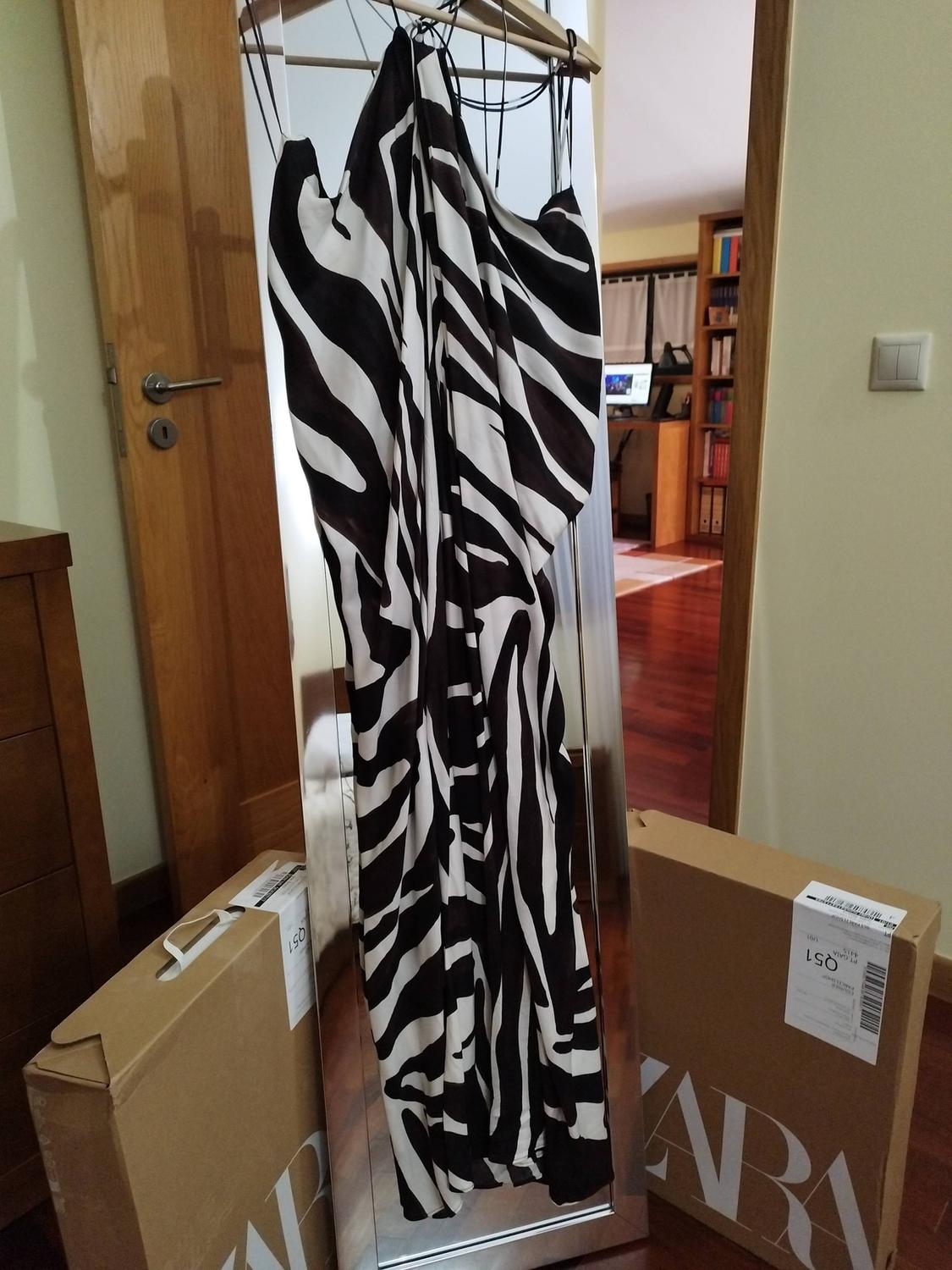 Zebra print dress in a mirror, surrounded by cardboard boxes with the Zara logo in a room with a wooden floor.