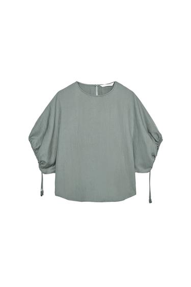 Front view of a sand-coloured blouse with a round neck, short adjustable puff sleeves and a rounded hem.