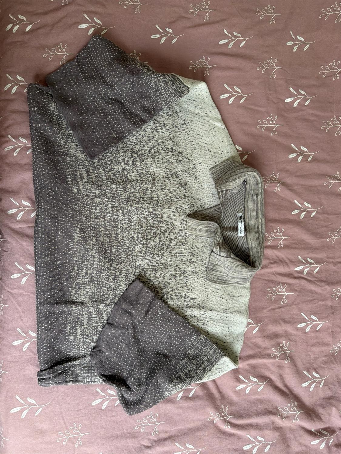 Mottled knit sweater with a gray and beige gradient polo collar, folded over pink fabric with white leaves. ZARA label visible.