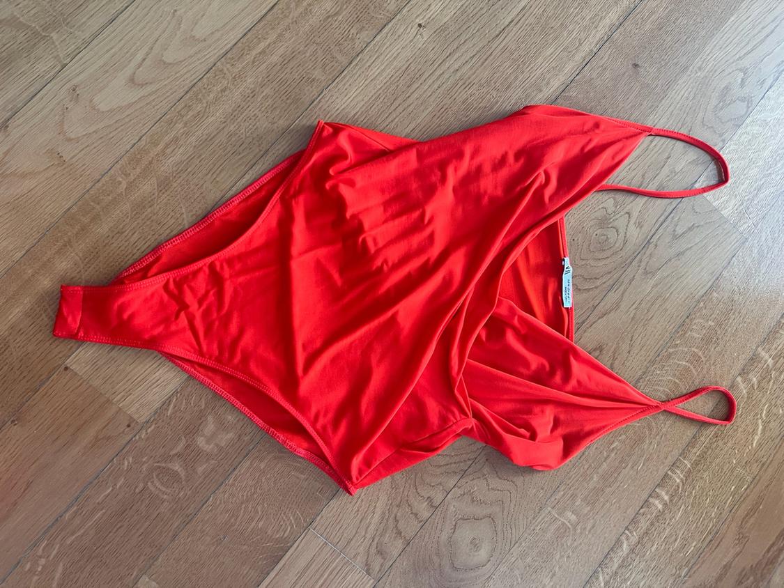 Red thin-strap bodysuit laid out on a light wood floor.