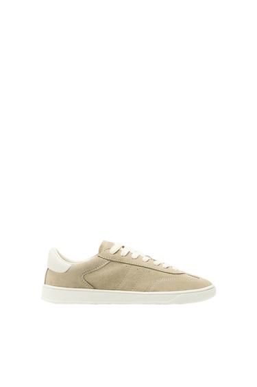 Beige suede trainer with white laces and white sole, side view on white background.