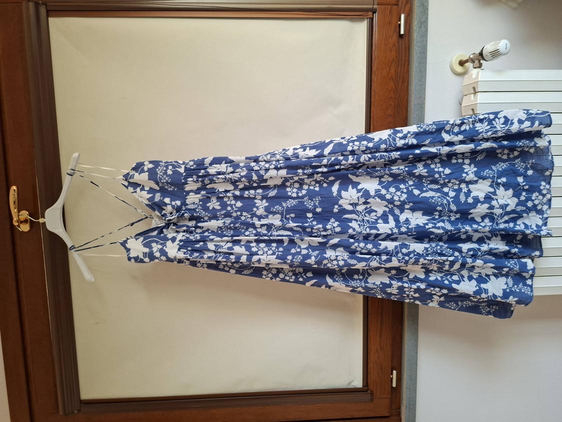 Blue dress with white floral print hanging on a hanger in front of a wooden window.
