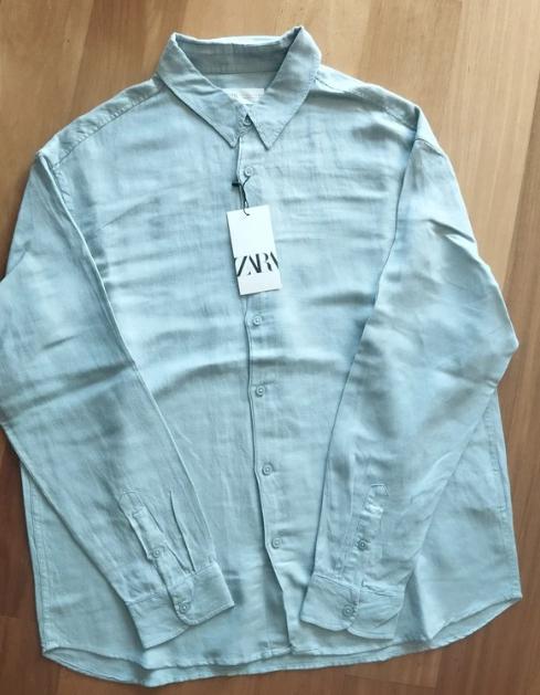 Light grey long-sleeved shirt on a wooden surface. Swing tag with the text "ZARA".
