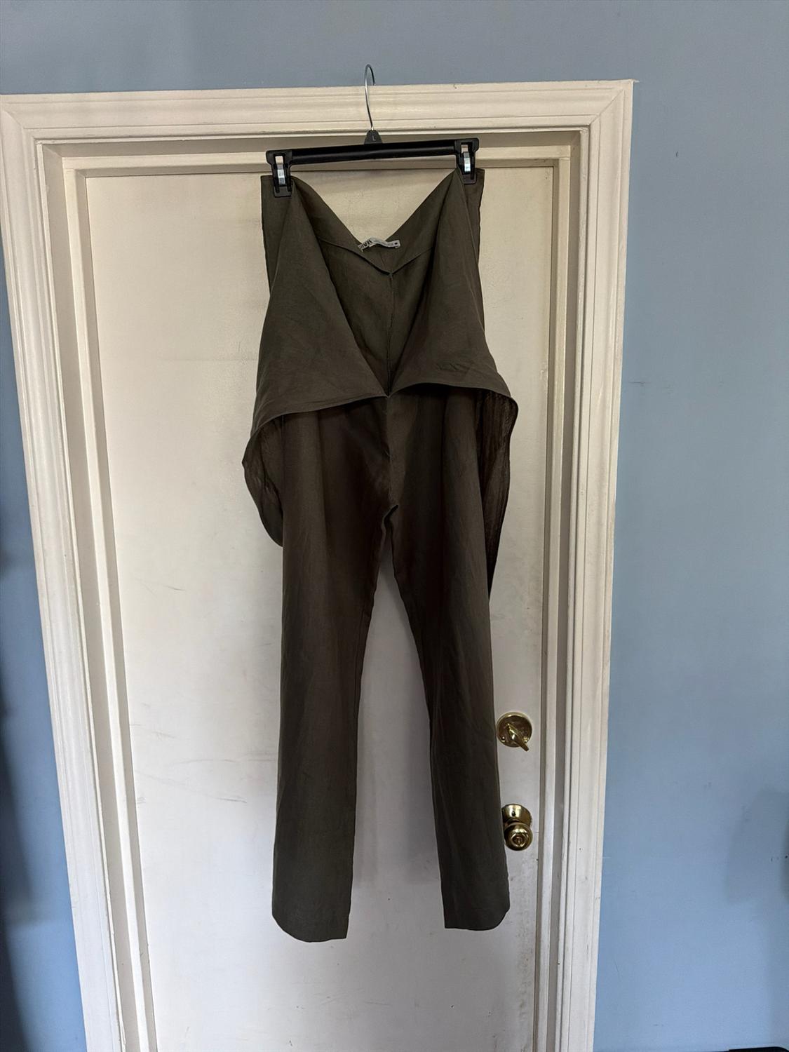 Dark green pants with a folded waistband, hanging on a hanger on a white interior door. Light blue wall background.