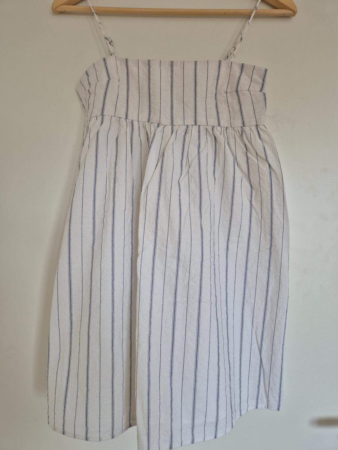 White dress with thin straps and blue vertical stripe print, hanging on a wooden hanger against a white background.