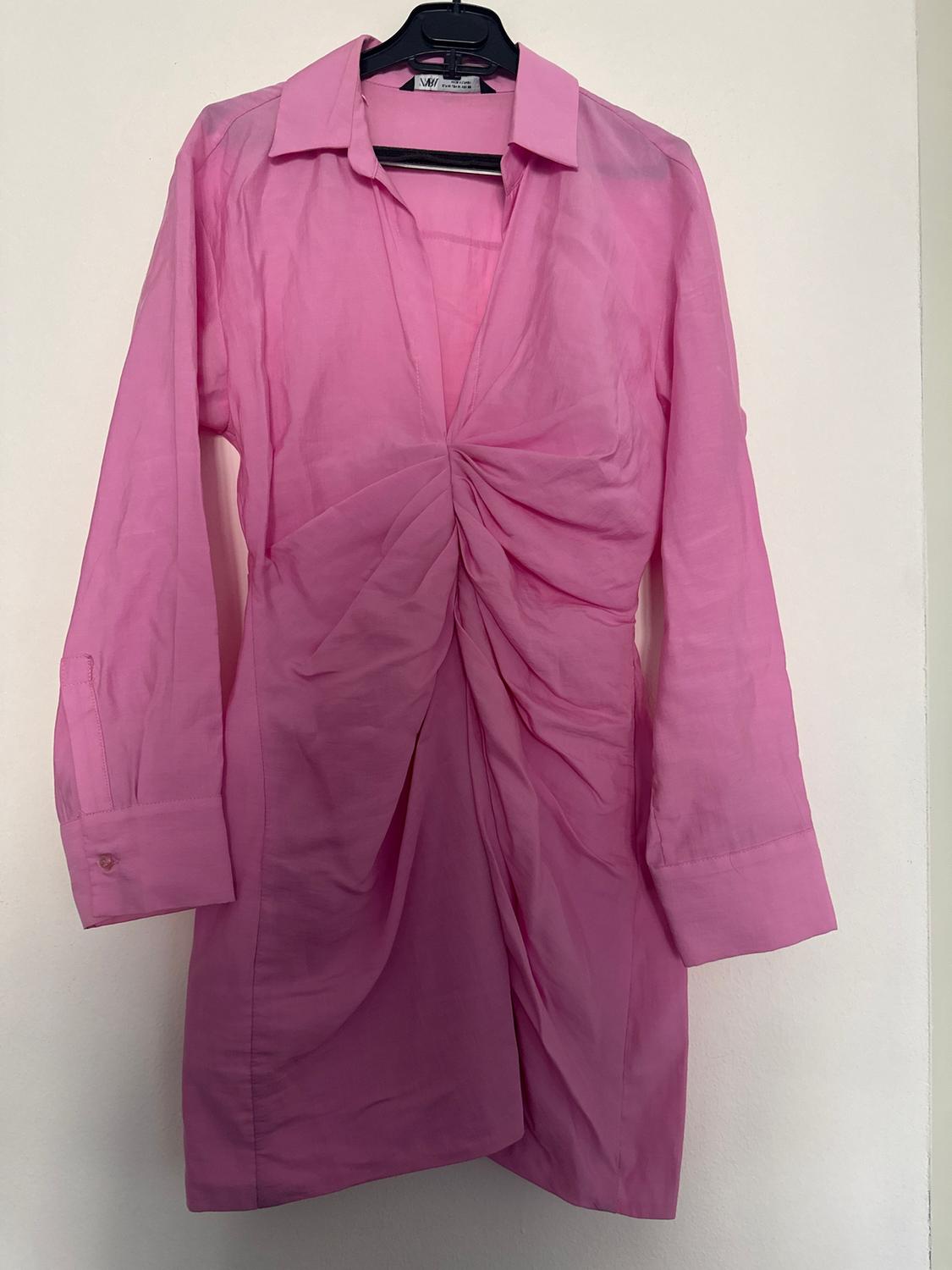 Long-sleeved pink dress with a classic collar and ruched detail on the front, hanging on a black hanger against a white background.