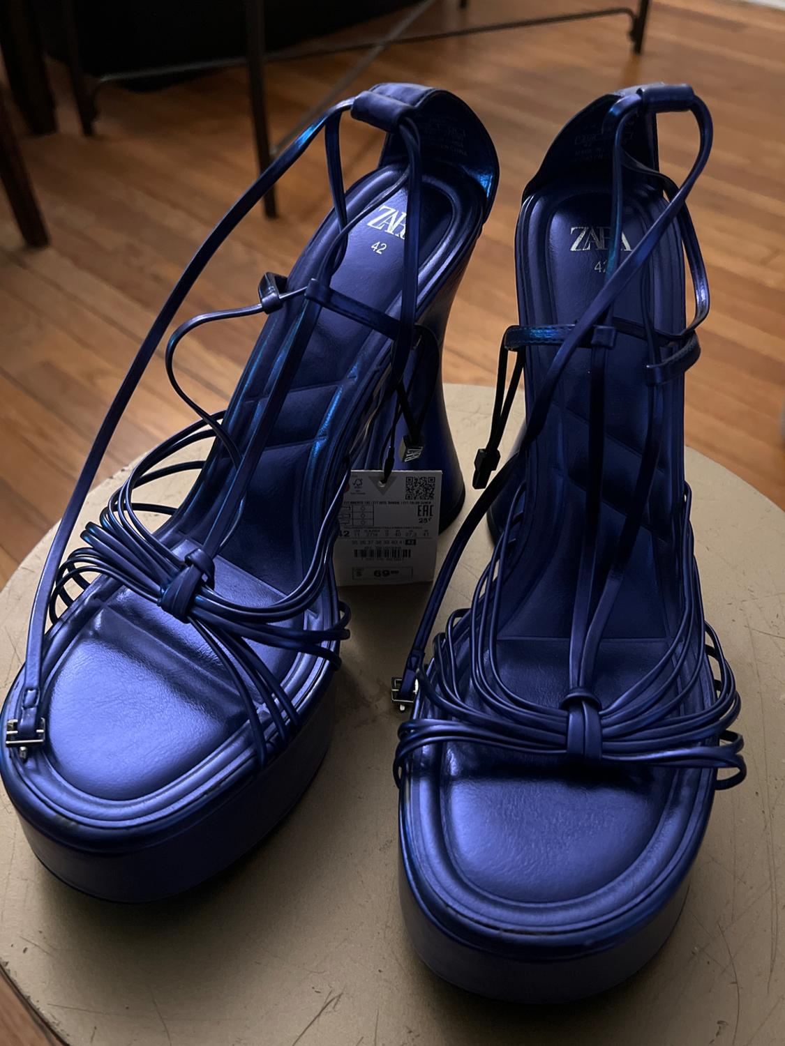 Blue platform sandals with thin straps and visible label, on a light wooden table.