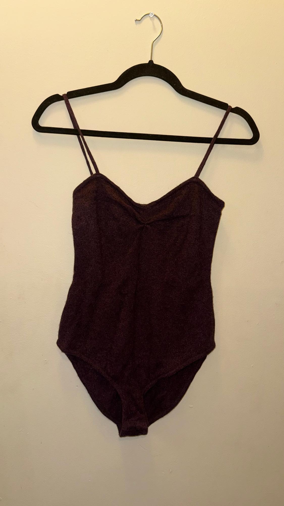 Burgundy spaghetti strap bodysuit hanging on a black hanger against a beige wall.