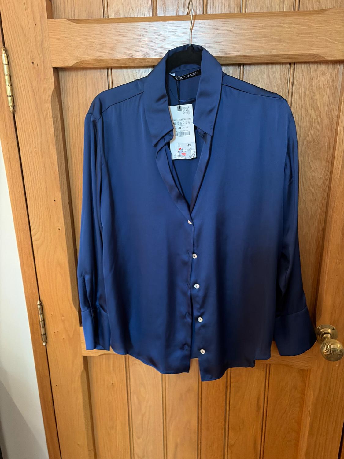 Blue satin shirt hanging on a wooden door, with label visible on the collar.