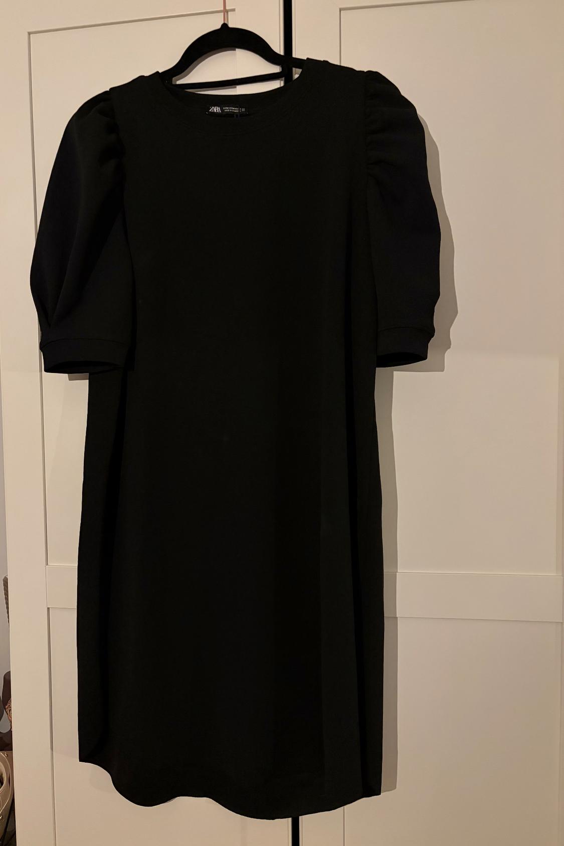 Black puff-sleeved mini dress hanging on a black hanger in front of a white wardrobe.
