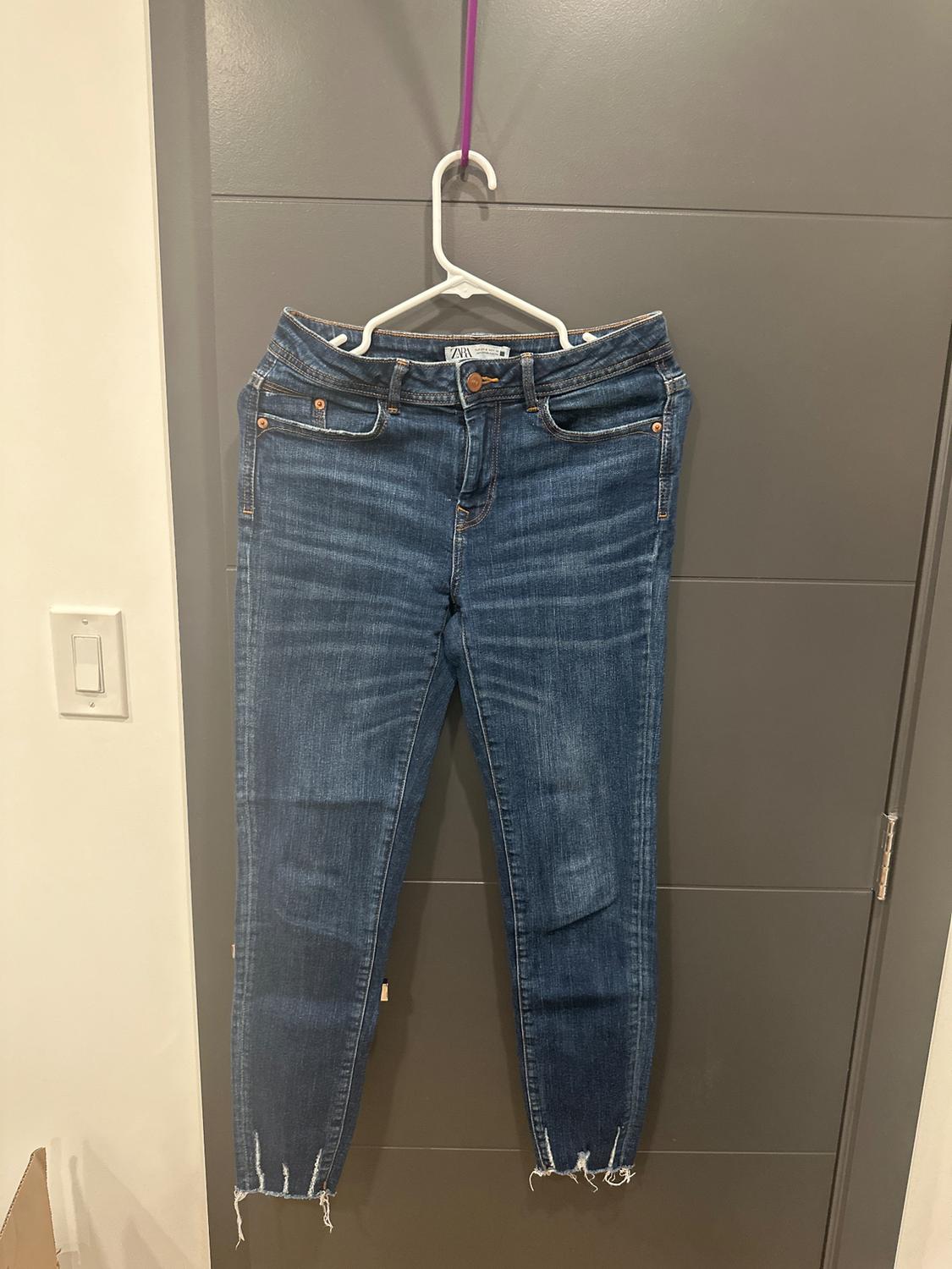 Worn blue jeans hanging on a white hanger with a purple hook, over a gray door.