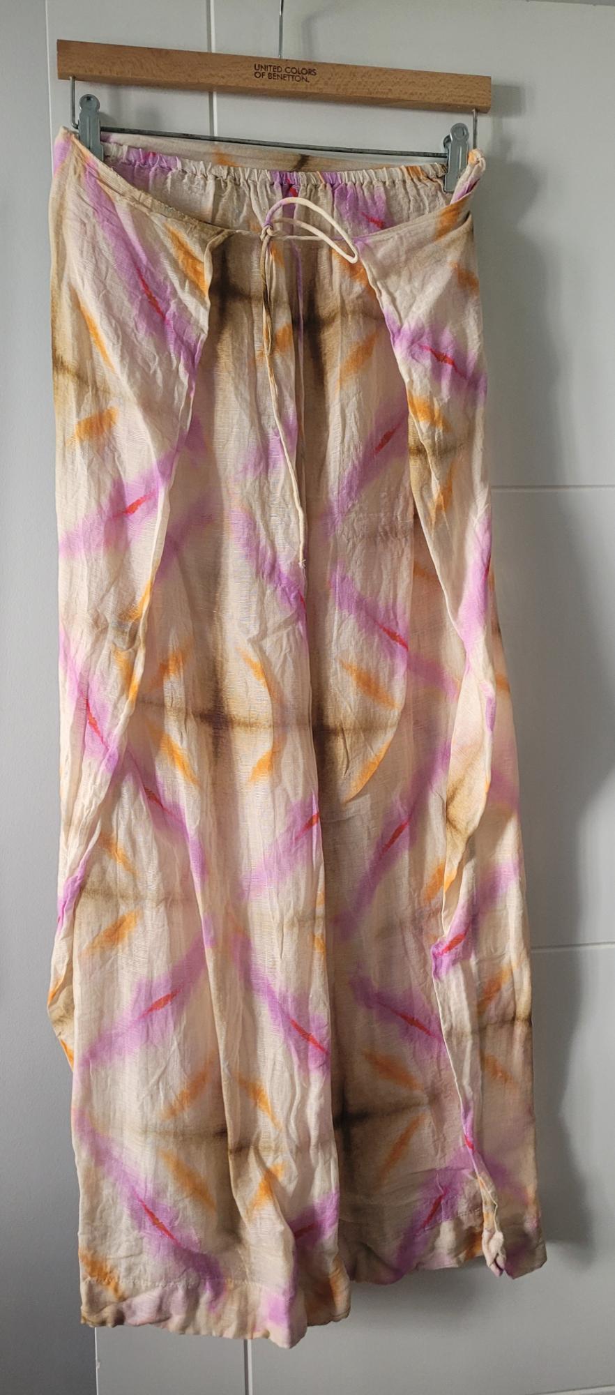 Lightweight fabric trousers with a pink and orange striped pattern, hanging on a United Colors of Benetton hanger.