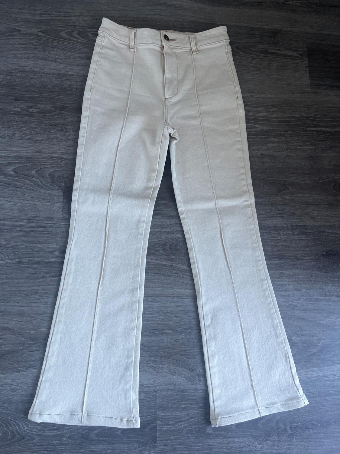 Beige flared trousers with visible seams, placed on a dark grey wooden floor.