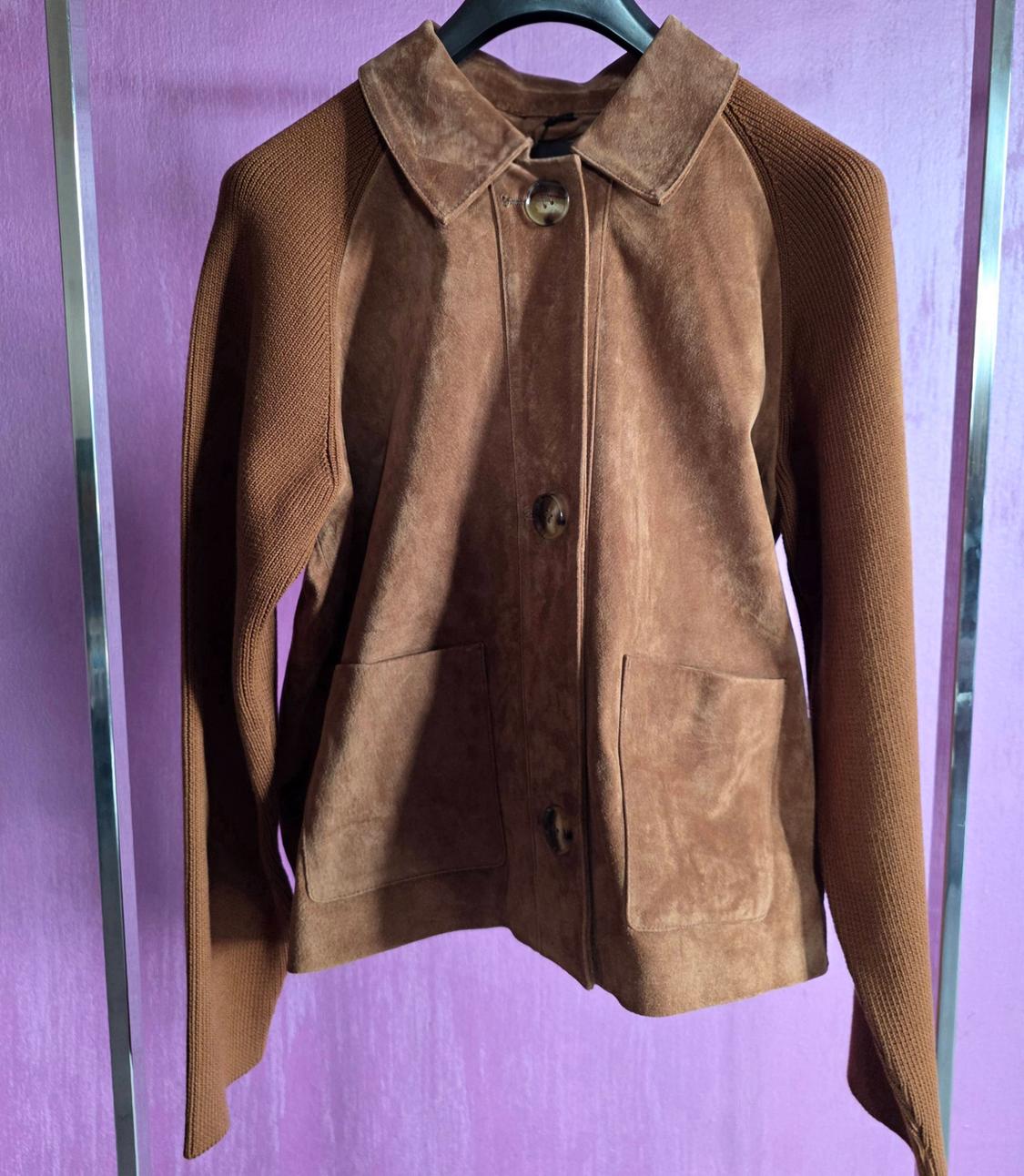 Brown suede jacket with knitted sleeves, hanging on a hanger against a purple background.