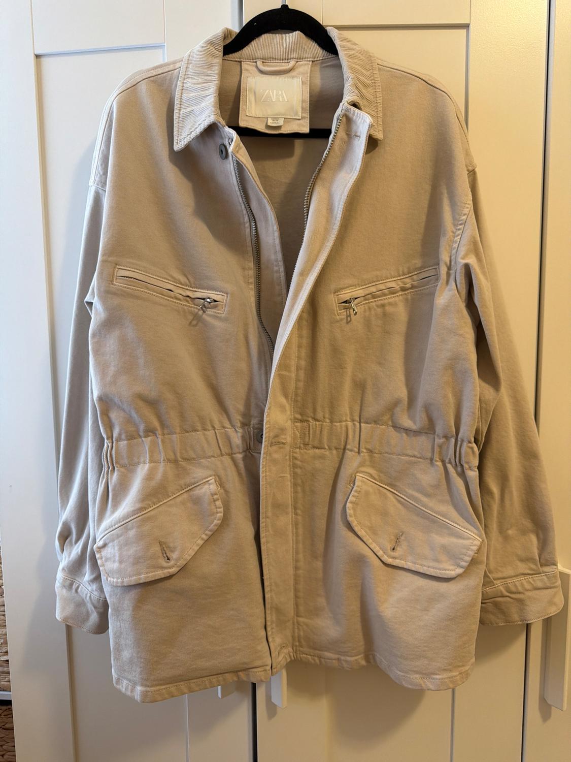 Beige casual jacket on a black coat hanger against a white door. It features a corduroy collar, pockets, a fitted waist, and a label with the text ZARA.