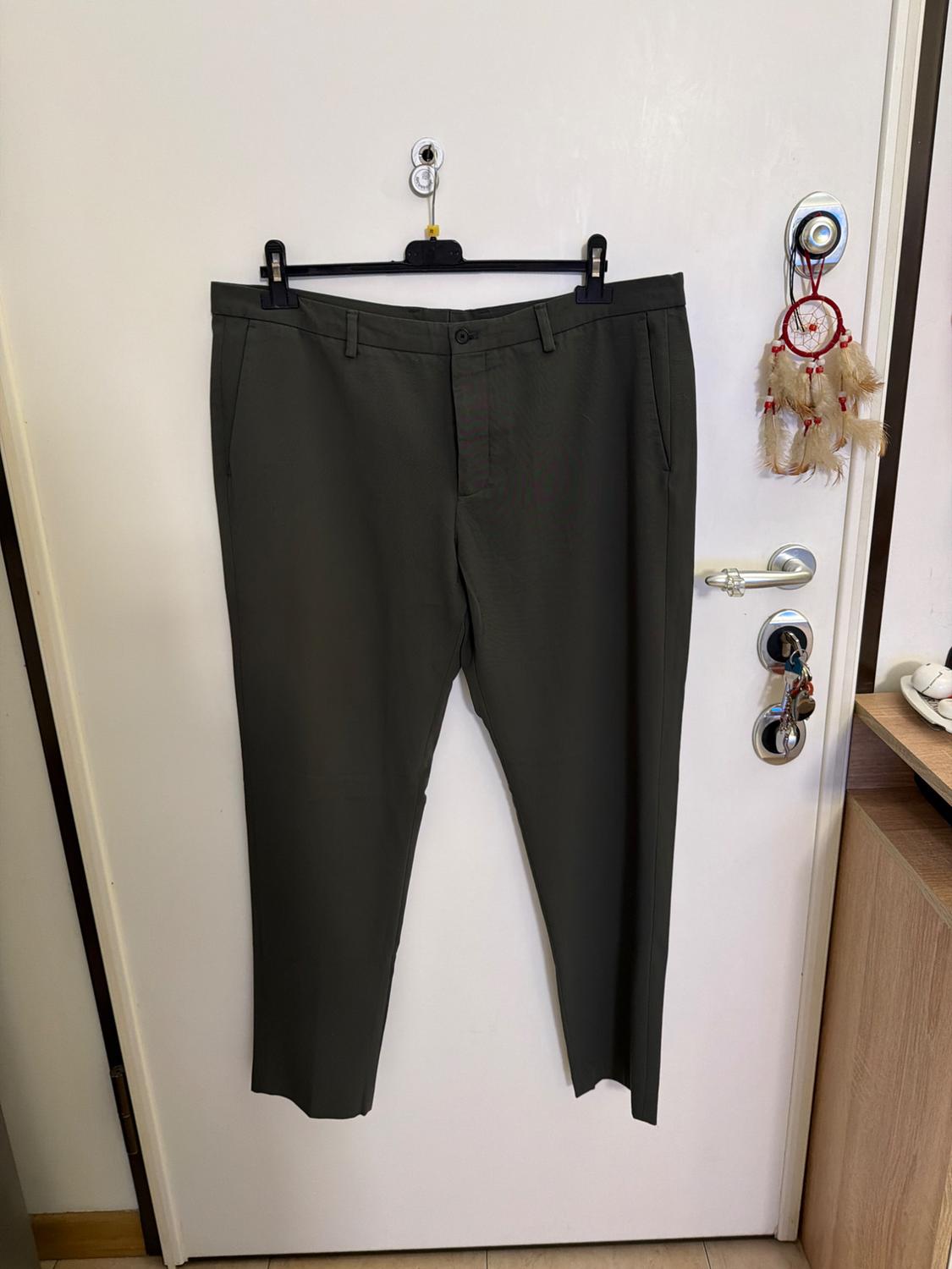 Grey trousers hanging on a black hanger over a white door. To the right, a dreamcatcher with feathers hangs from the handle.