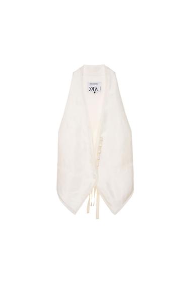 Sleeveless white vest with front buttons and dangling ties. Visible tag with "ZARA" text on the inside of the collar.