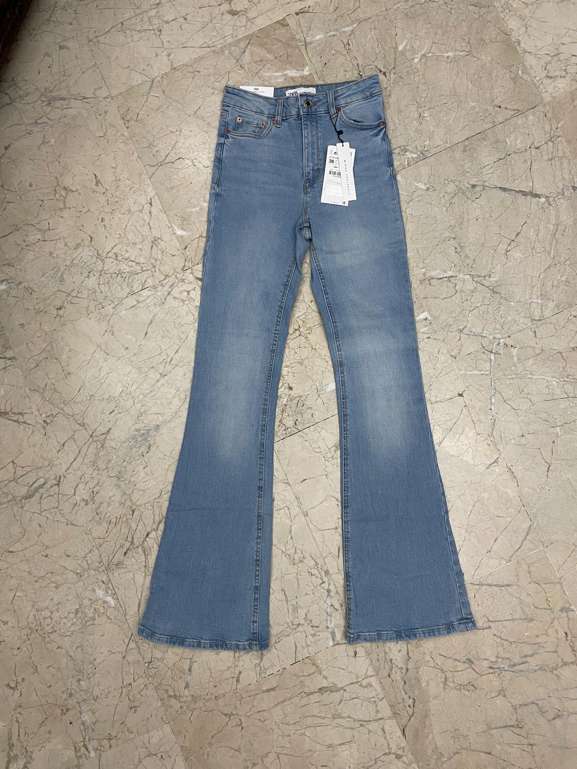 Light blue denim flared jeans with hang tags, placed on a beige marble floor.