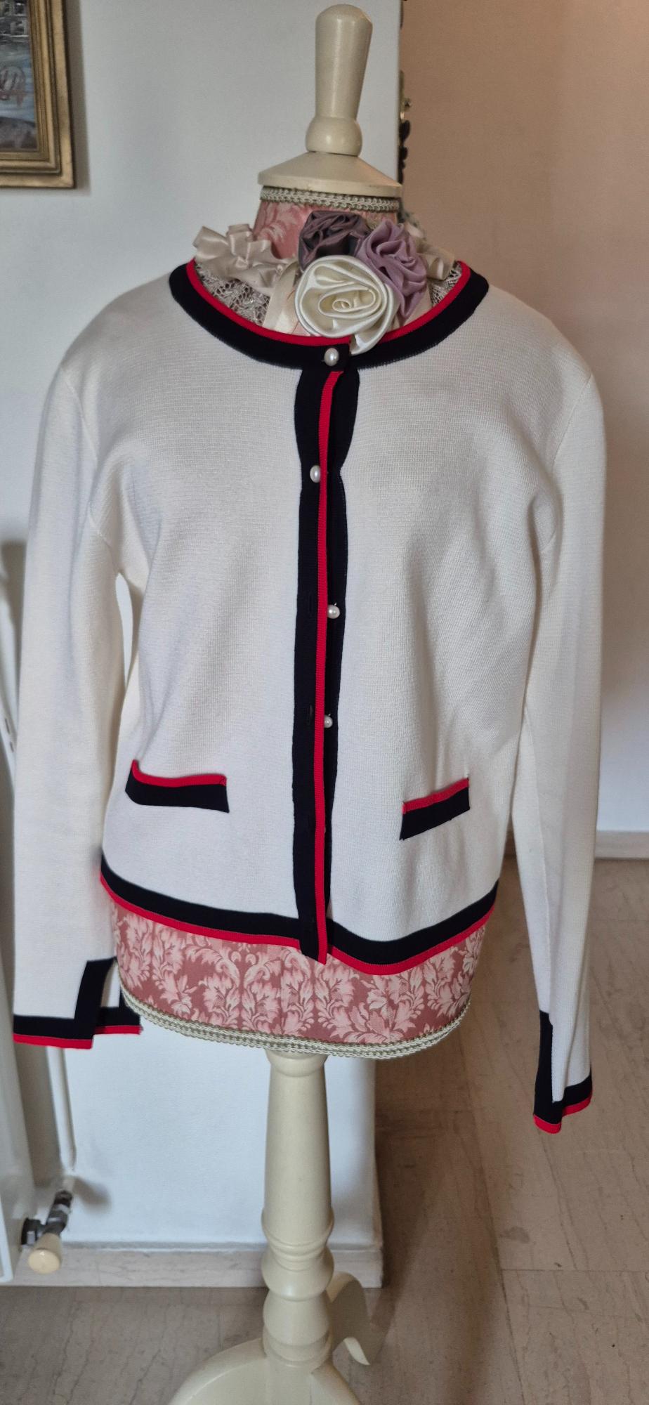 Mannequin with white button-up jacket, black and red trim, over a pink blouse with floral print and flower details on the collar.