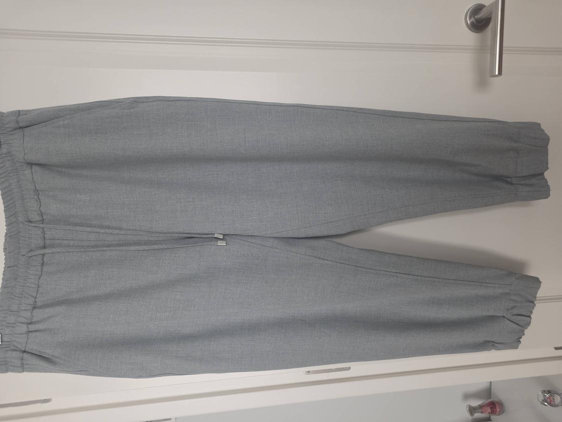Grey trousers hung on a white door, with an elasticated waist and ankles. Simple, minimalist background.