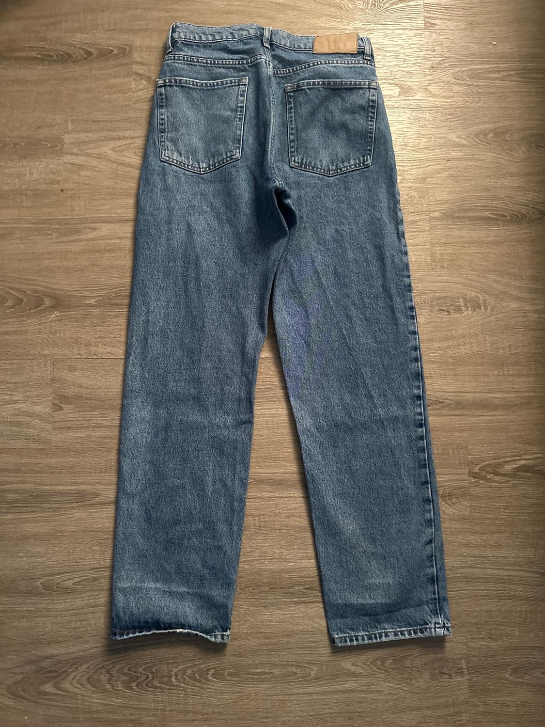 Straight-cut blue jeans seen from behind, with two back pockets, on a light wooden floor.