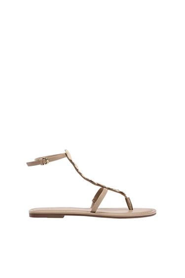 Beige flat strappy sandals, featuring round metallic details, a buckle fastening and the word ZARA on the insole, against a white background.