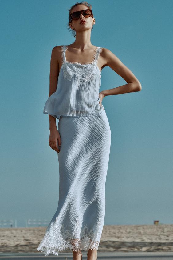 Souprava světle modrého topu a sukně s krajkou na výstřihu a lemu, širokými ramínky a plisovanou texturou.