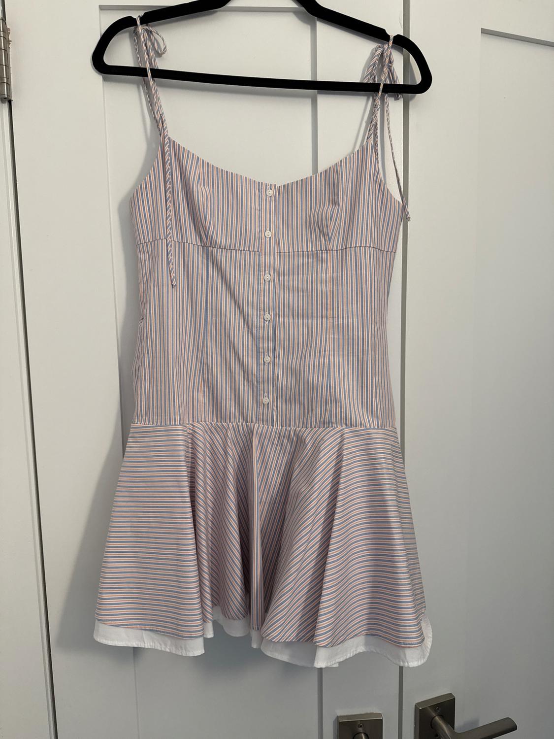 Sleeveless dress with buttons and a vertical blue and red striped print, hanging on a black hanger over a white door.