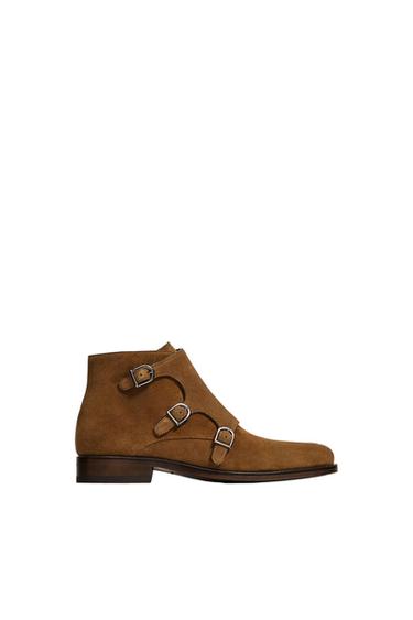Brown suede boot with three metallic buckles on the side, dark leather sole, on a white background.